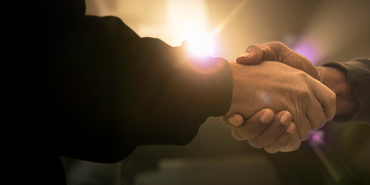 two men shaking hands with a bright light in the background
