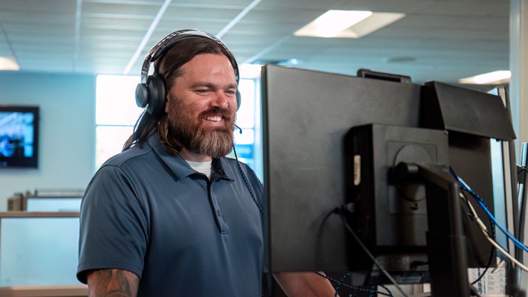 A J.B. Hunt agent wearing a headset and smiling while assisting a customer from a modern office workstation.