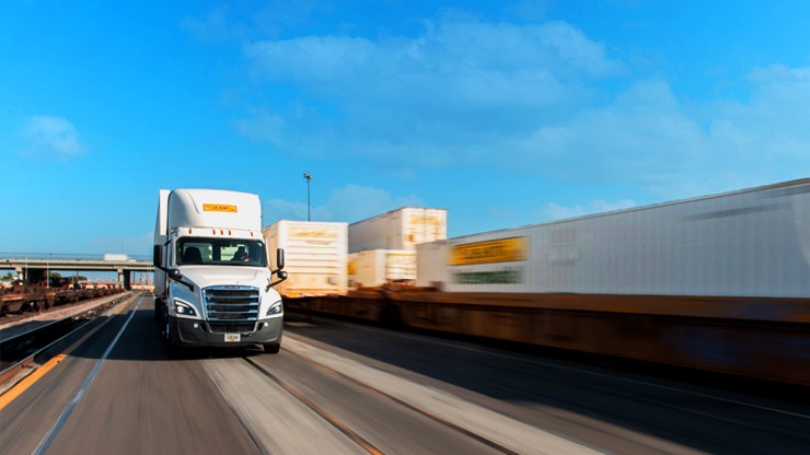 A J.B. Hunt semi-truck driving on the highway alongside freight trains, representing efficient logistics and transportation solutions.
