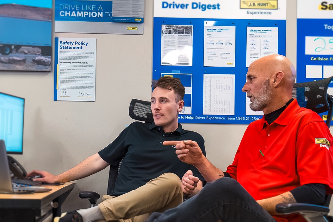 Fleet Management Experts Discuss Custom KPIs at J.B. Hunt Two J.B. Hunt employees discussing custom fleet management KPIs in an office with safety and driver performance materials on the wall.