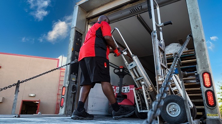 JB Hunt dedicated logistics driver loading temperature-controlled freight into a refrigerated trailer using a pallet jack.