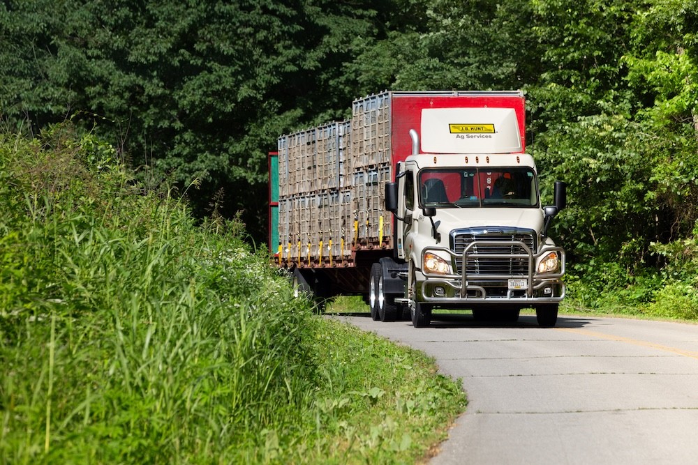 A J.B. Hunt Ag Services truck hauls stacked live haul crates on a rural road, illustrating flexible logistics management during a pop-up fleet operation.
