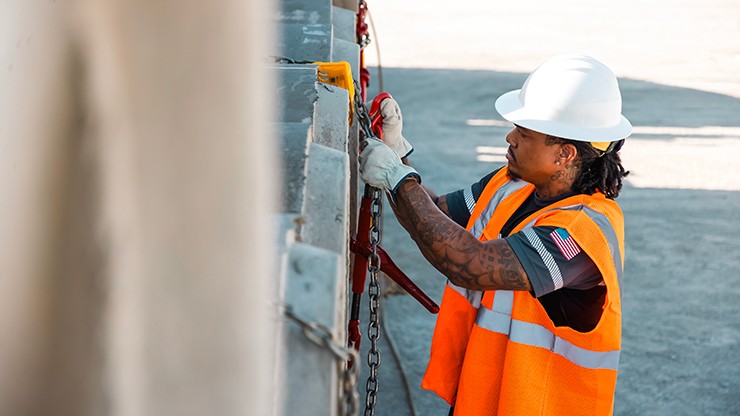 J.B. Hunt truck driver in safety vest and hard hat securing cargo with a chain on a flatbed trailer