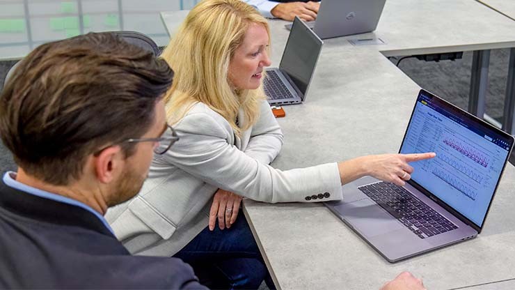 Business professionals discussing fleet data integration, with a woman pointing at a laptop displaying analytics in a meeting setting.