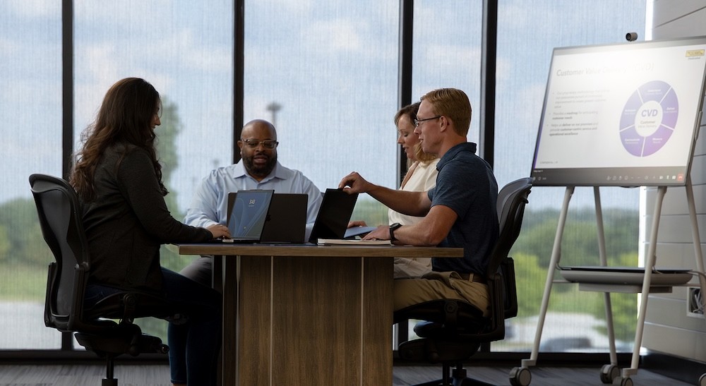 four people meet in a conference room that also has a smart screen