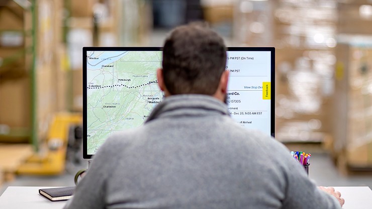 A customer in a warehouse monitors a digital map on a computer screen to track shipments.