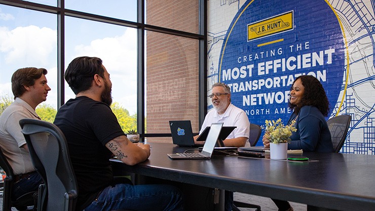 Four people meeting in a conference room with laptops. 