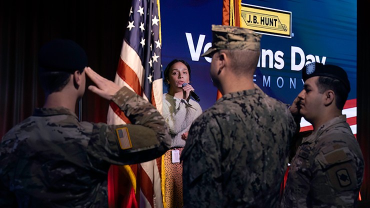 Military members saluting the American flag while woman sings national anthem