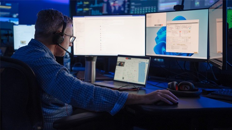 J.B. Hunt employee monitors multiple computer screens in a dark, high-tech security operations center to prevent cargo theft.
