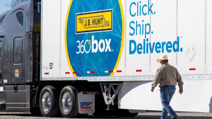 A J.B. Hunt 360° Box trailer with “Click. Ship. Delivered.” branding is parked, while a man wearing a cowboy hat and beige shirt walks past it.