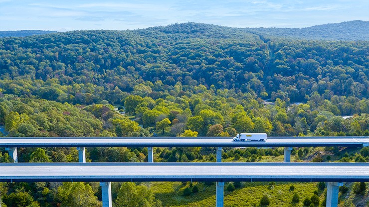 Photo of a J.B. Hunt semi truck and trailer crossing a bridge over a hilly landscape