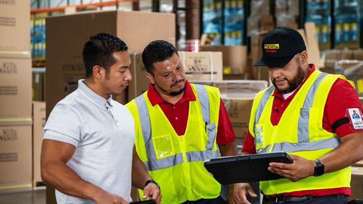three individuals look at a digital tablet in a warehouse