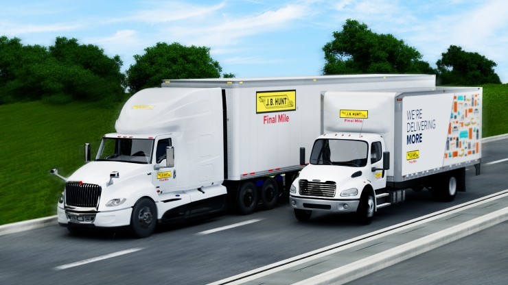 Two J.B. Hunt Final Mile delivery trucks driving side by side on a highway. The truck on the left is a larger semi-truck, while the truck on the right is a smaller box truck with colorful graphics and the text 'We're Delivering More' on the side. Both trucks are branded with J.B. Hunt Final Mile logos and are traveling along a road bordered by green trees and grass under a clear blue sky.