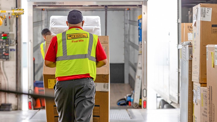 Final mile driver loads a large box into a truck with a hand cart
