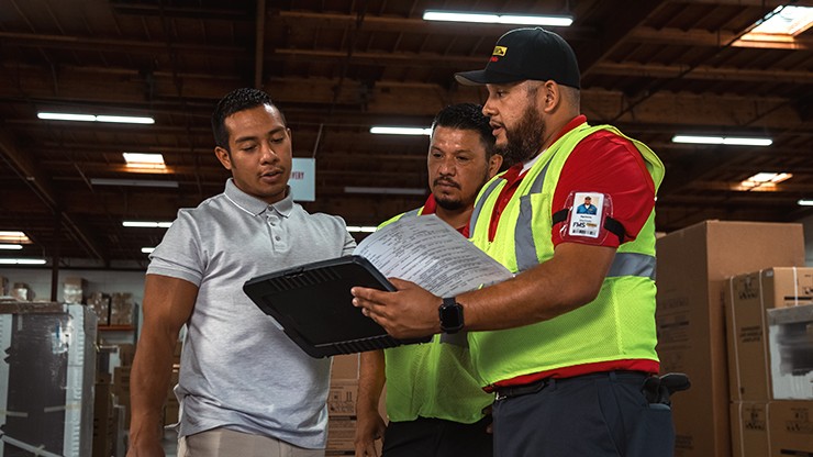 Three men looking at paperwork inside a warehouse