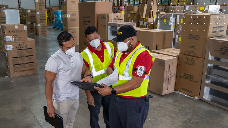 three men working in warehouse looking at tablet