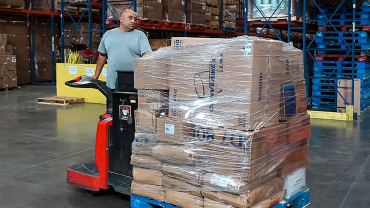 man driving pallet jack through warehouse man driving pallet jack through warehouse