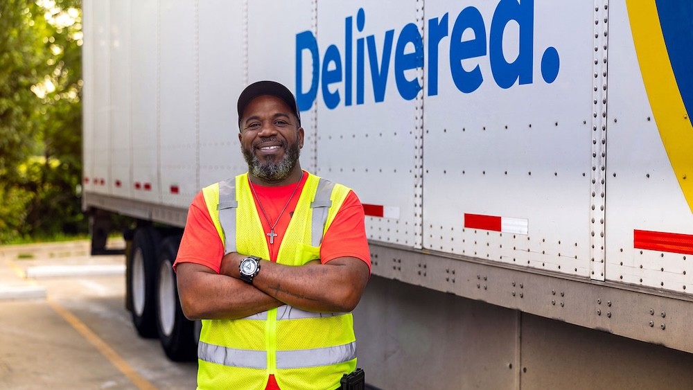 Carrier standing in front of a J.B. Hunt trailer with “Delivered” branding, representing freight carriers who choose to become a carrier with J.B. Hunt for reliable loads, flexible options and Carrier 360 technology.