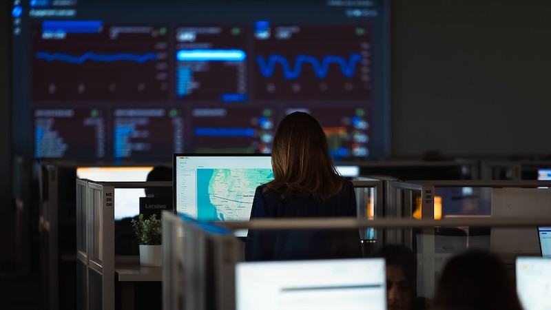 A person works at a computer in an operations center while large wall-mounted dashboards display real-time performance metrics, maps and analytics. The environment represents the use of automation, AI and visibility tools that help shippers, carriers and JB Hunt teams streamline workflows and improve decision making.
