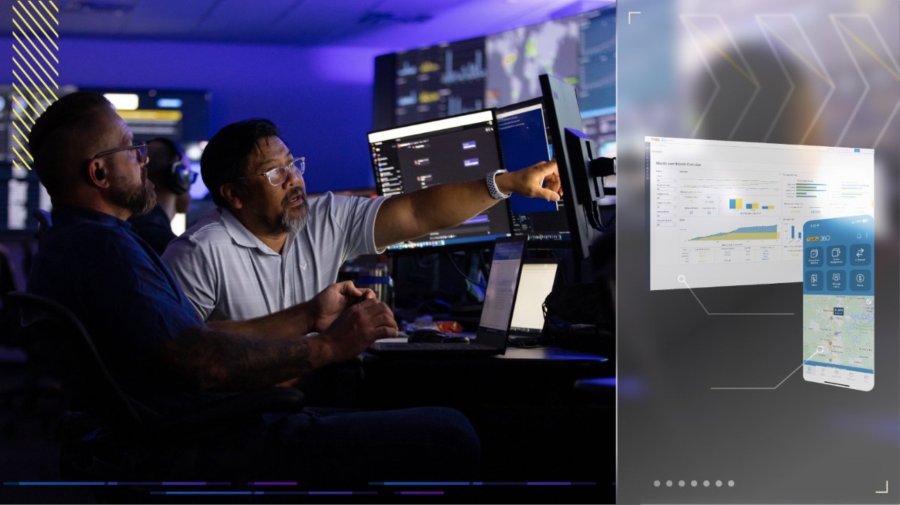 Control Room Data Analysis Technology in Action: Data-Driven Two men in a control room analyzing data on multiple computer screens, with a projection showing data analytics and a mobile app interface.
