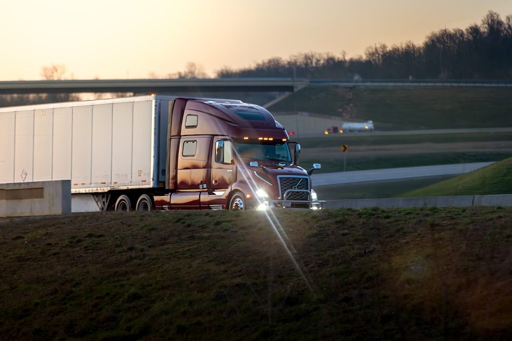 Maroon semi-truck hauling a trailer on an elevated highway during sunset, highlighting carrier partnerships and transportation infrastructure.