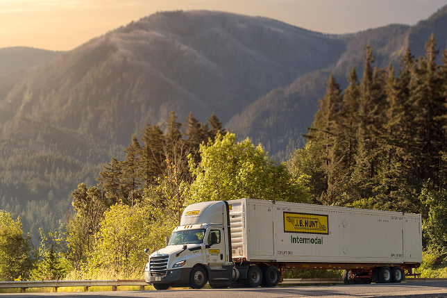 A J.B. Hunt intermodal truck on the highway with mountains in the background. 