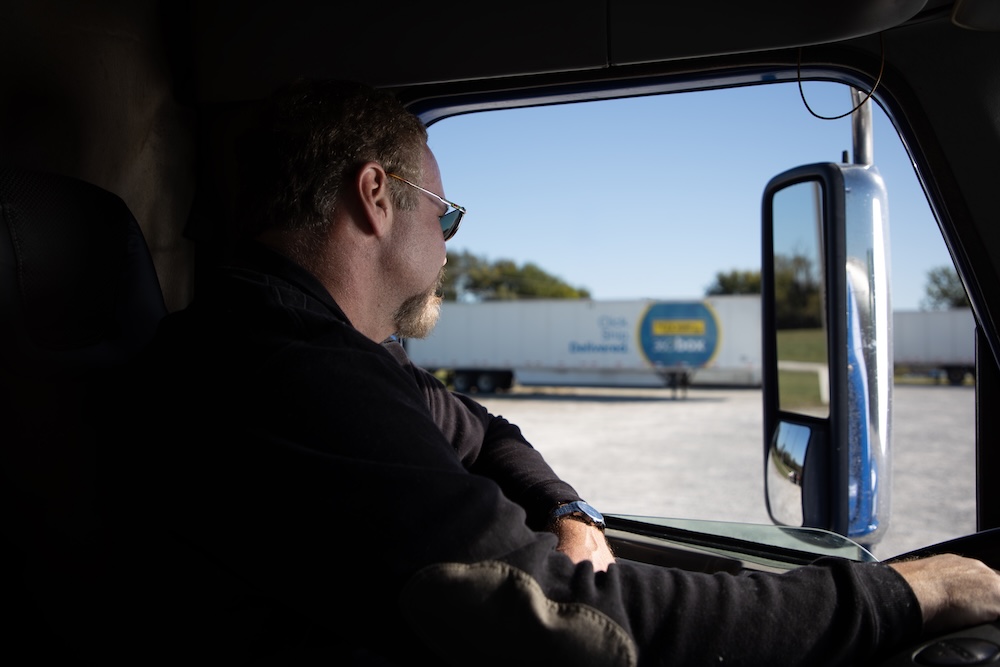 Individual inside a truck cab looking out toward parked trailers, symbolizing independence and opportunities for owner-operators in freight transportation.