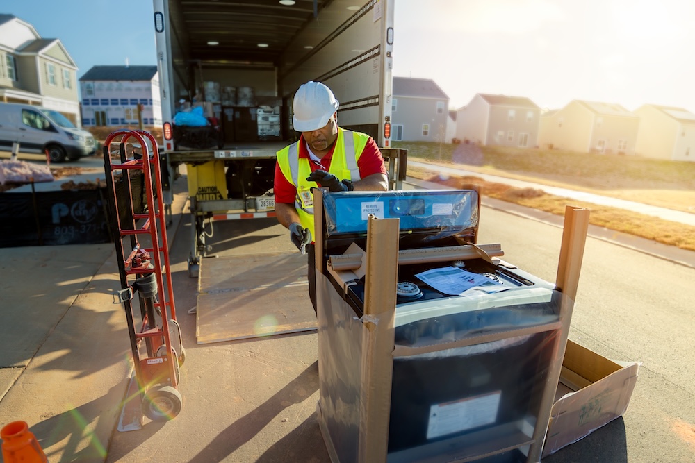 J.B. Hunt employee in safety vest unloading large appliance from truck in residential area, showing final mile delivery.