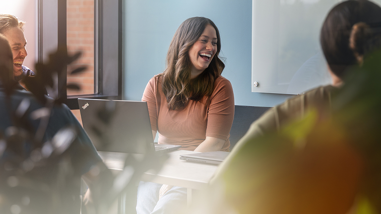 Person sitting at a conference table with a laptop during a team meeting in a modern office setting.
