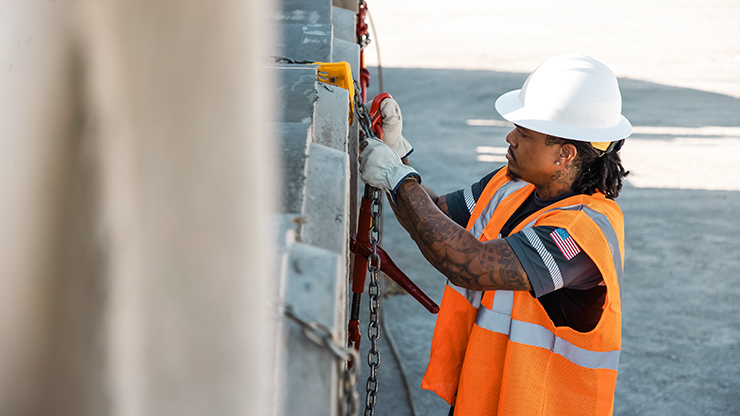J.B. Hunt truck driver in safety vest and hard hat securing cargo with a chain on a flatbed trailer