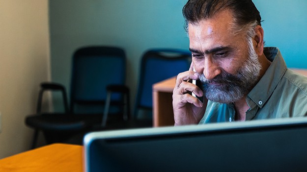 Business professional speaking on the phone while working at a computer desk in an office setting.