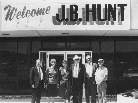 black and white photo of Johnelle and J.B. Hunt with others in front of a welcome banner
