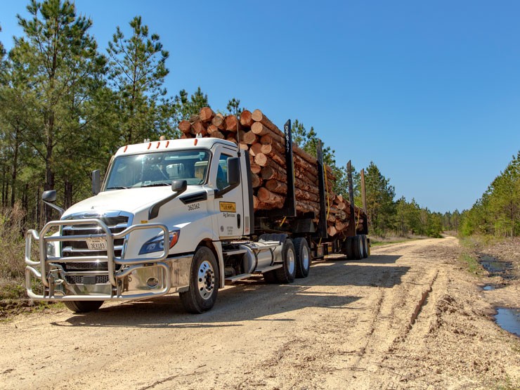 Ag Services truck loaded with logs driving down a dirt road