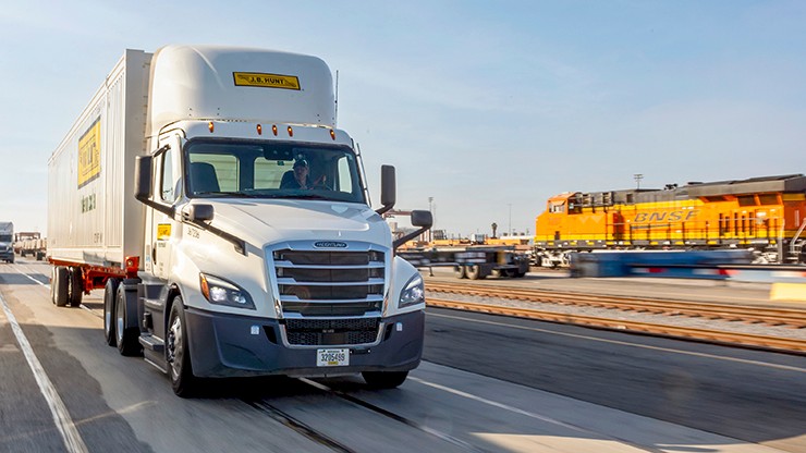 J.B. hunt tractor trailer driving past a BNSF train
