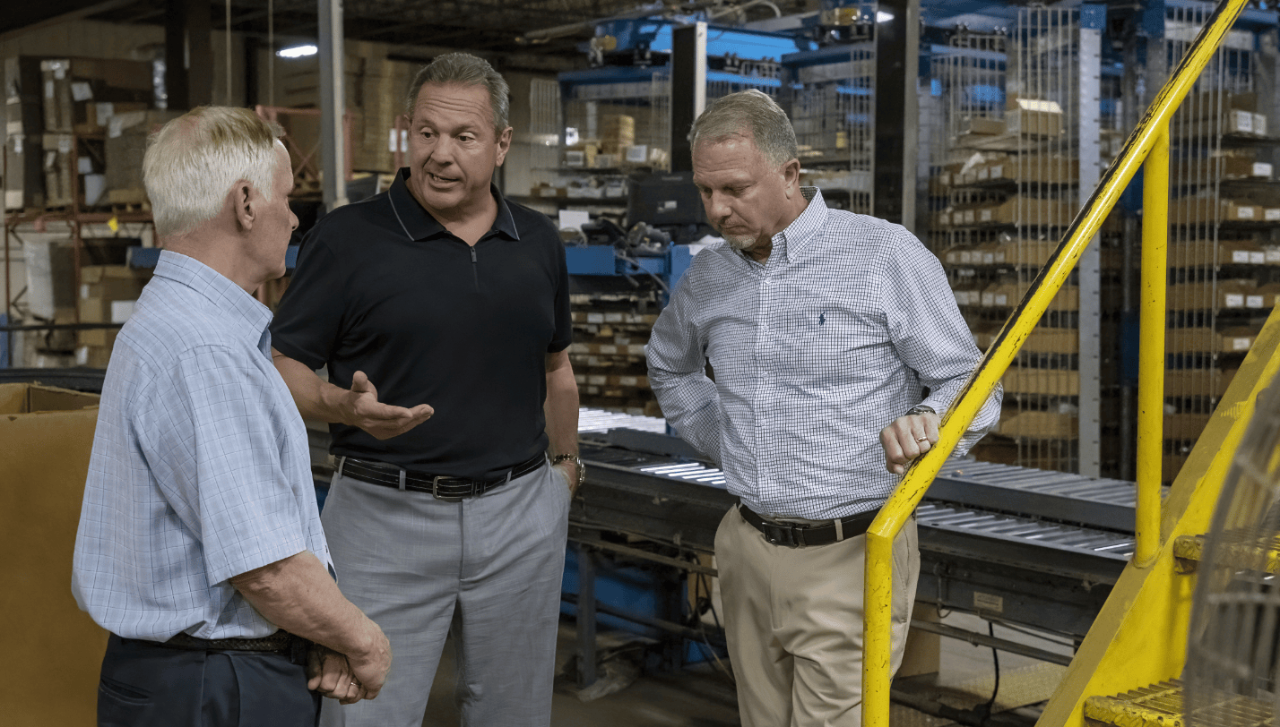 Three individuals converse in the Bostwick-Braun warehouse