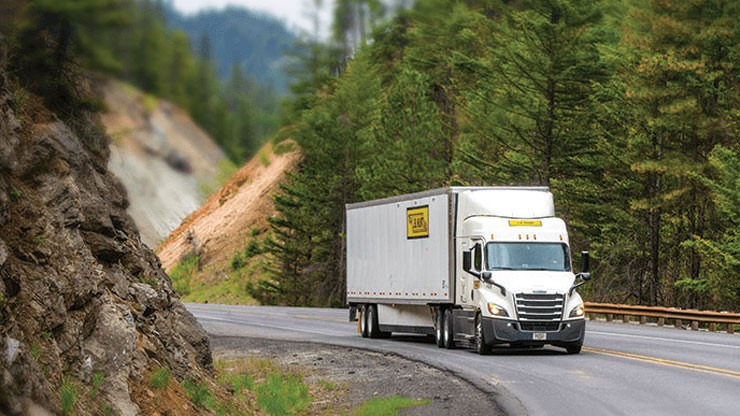 A J.B. Hunt semi truck travels up a two lane mountain highway