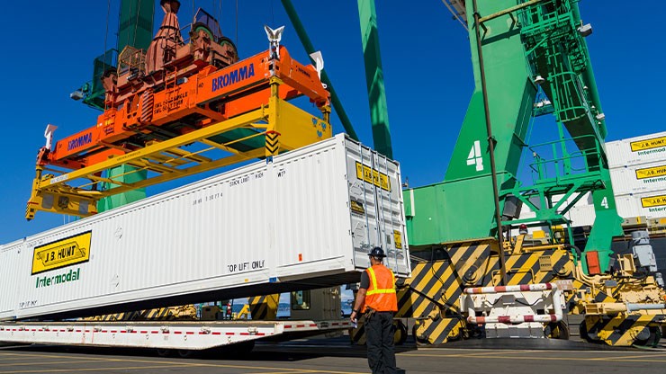 a crane lifts a J.B. Hunt Intermodal shipping container off of its flatbed trailer