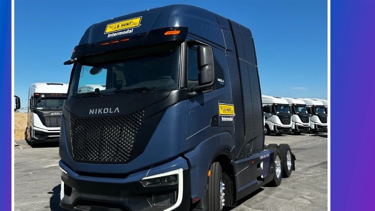 A fleet of Nikola electric semi-trucks, branded with J.B. Hunt’s Intermodal logo, parked in an industrial lot A fleet of Nikola electric semi-trucks, branded with J.B. Hunt’s Intermodal logo, parked in an industrial lot