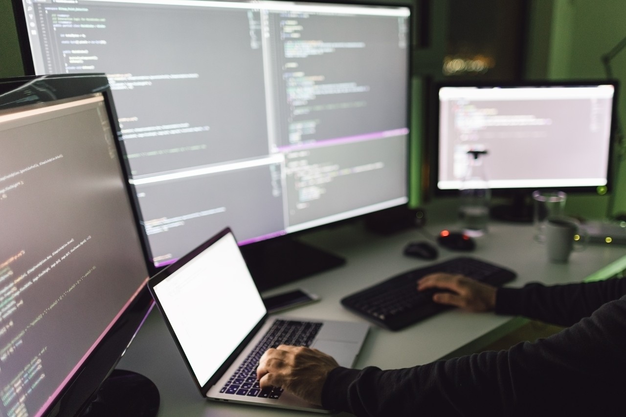 photo of cyber security employee using a laptop and monitors