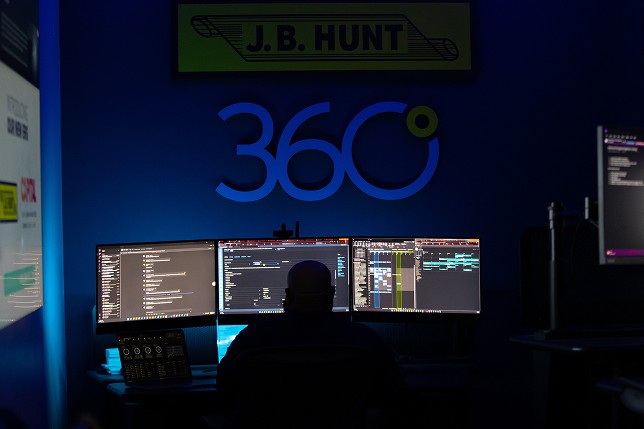 A J.B. Hunt employee works with three monitors in front of him. 