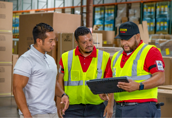 two warehouse workers showing a customer something on a tablet inside of a warehouse