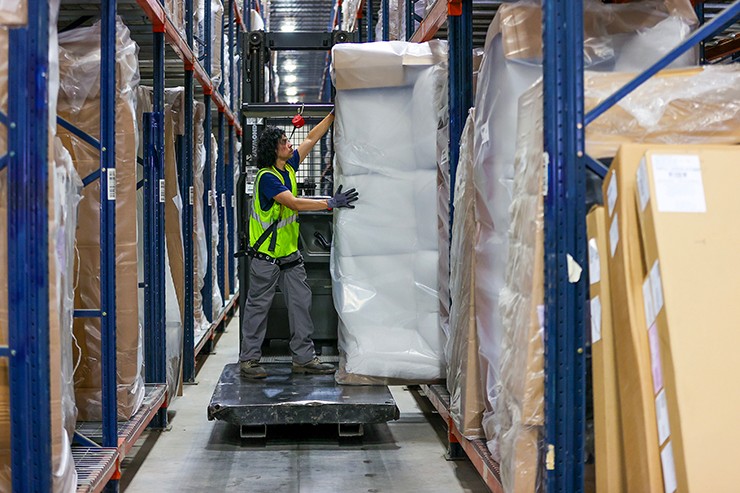 Warehouse employee moving furniture onto forklift.