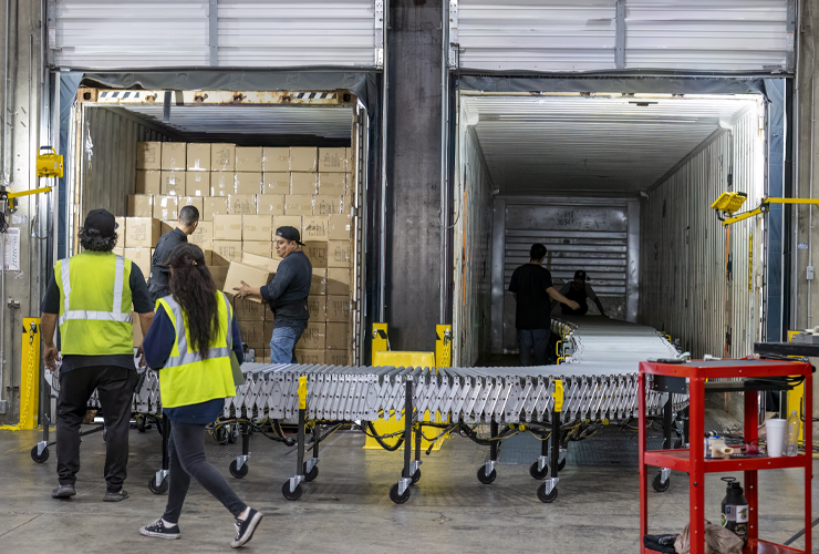 employees moving boxes from one trailer to another using a conveyor