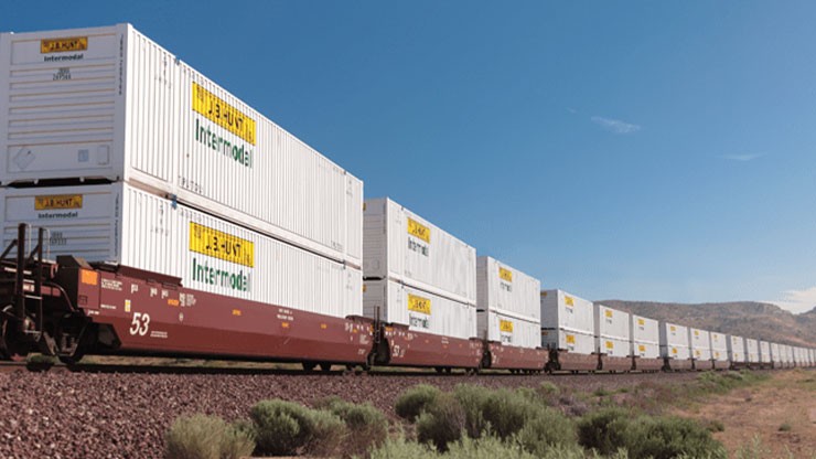 Long intermodal freight train carrying stacked white shipping containers labeled “Intermodal” on flatcars through a dry, desert landscape under a blue sky.