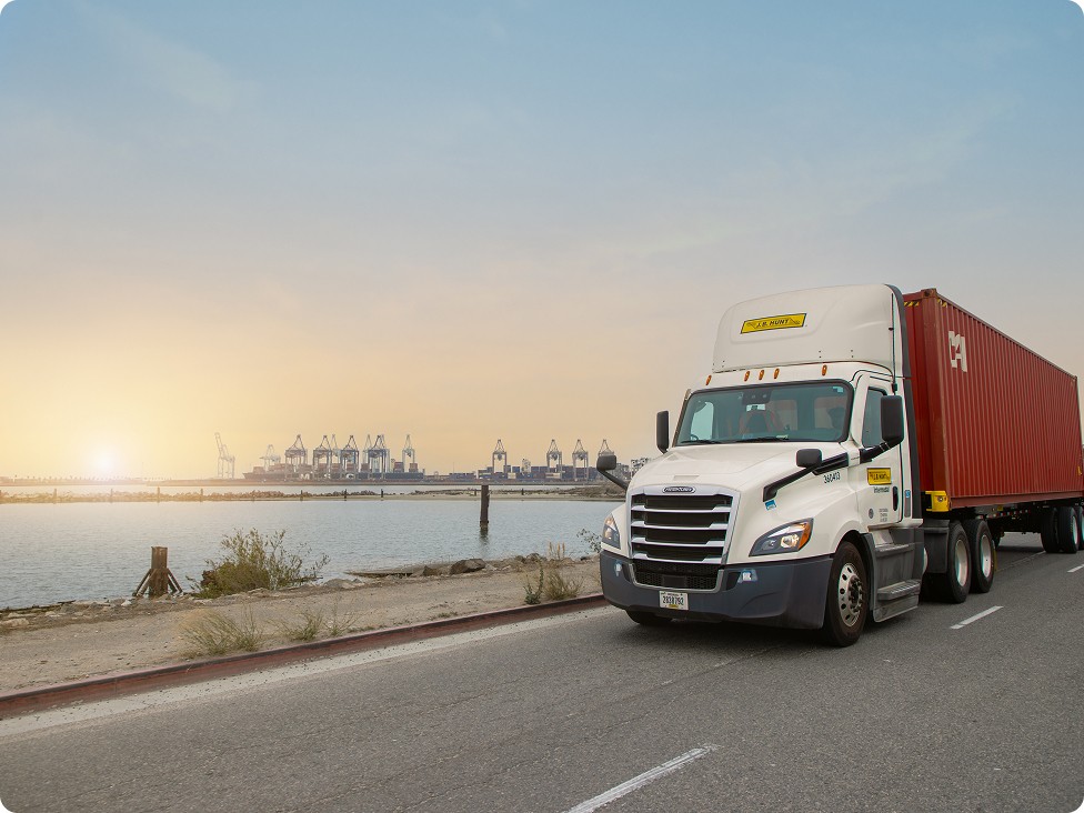 J.B. Hunt tractor pulling a container with a port in the distance