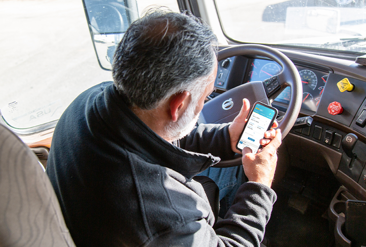 A truck driver sits behind the wheel of a truck and opens the J.B. Hunt Carrier 360 app on their phone